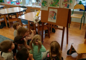 Dzieci siedzą przed tablicą, oglądają ilustracje do legendy „O smoku wawelskim”